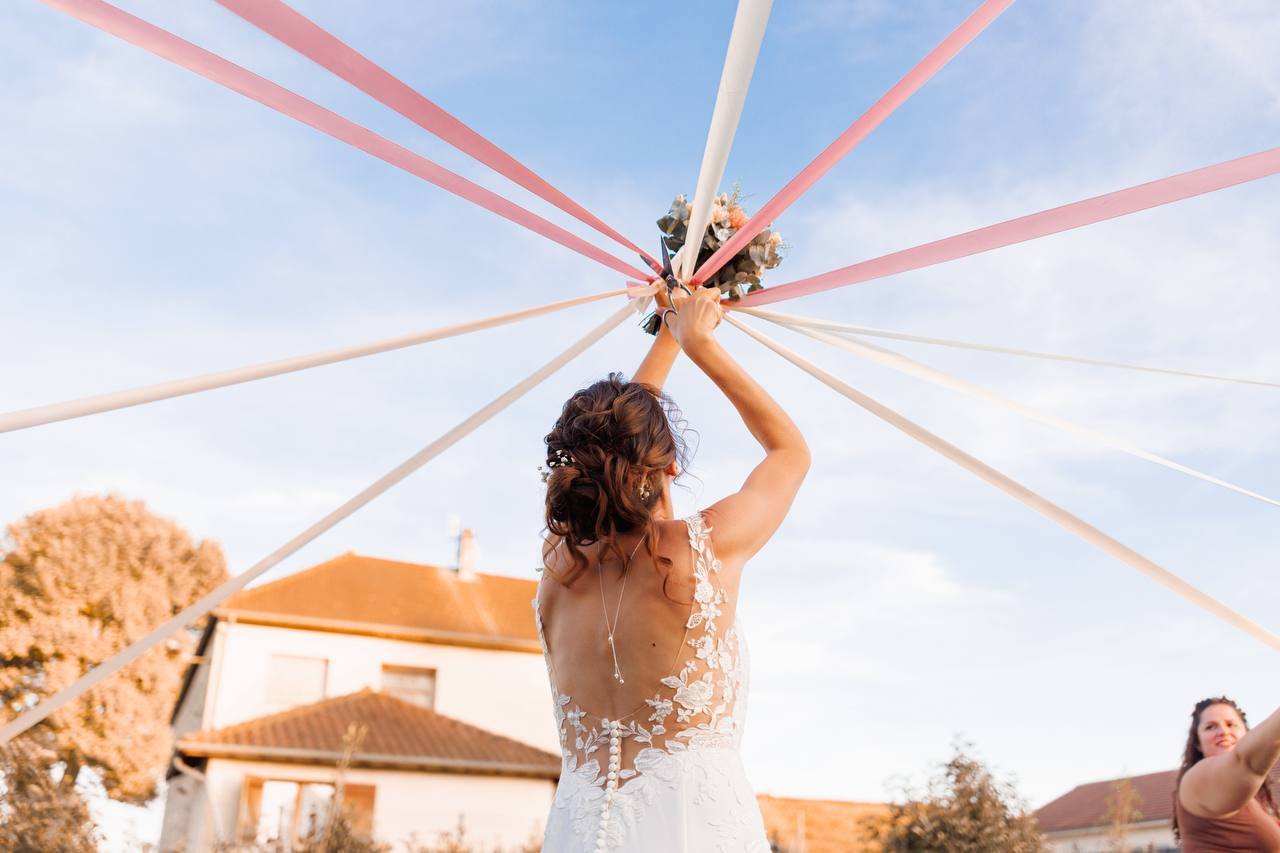 La mariée de dos lève le bouquet, les rubans partent vers le ciel